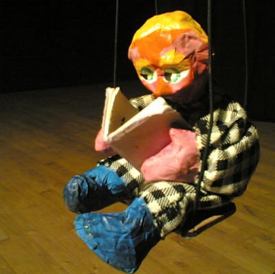 un petit bonhomme, de papier mâché, assis sur une balançoire est plongé dans sa lecture.